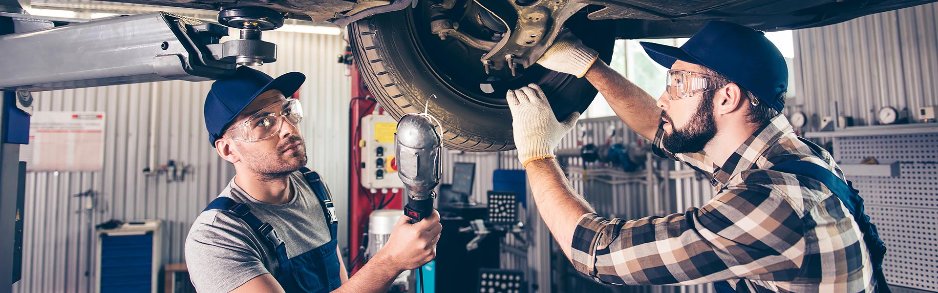 Auto technicians performing a suspension and steering inspection under a lifted vehicle