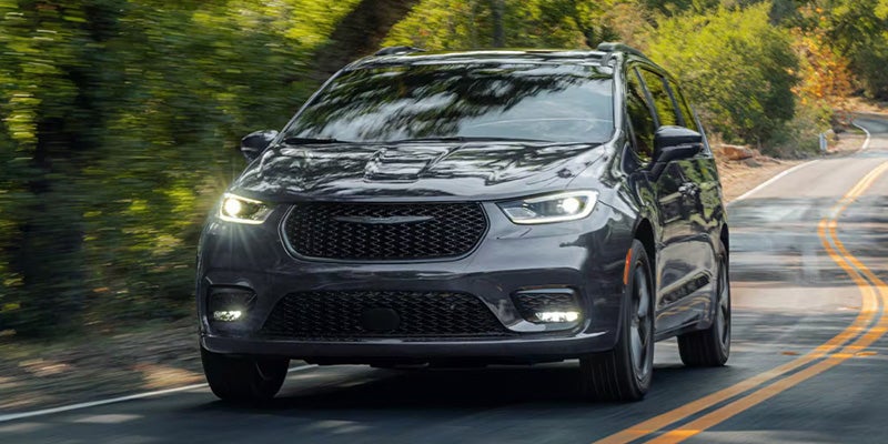 Gray minivan driving on a curved road surrounded by greenery