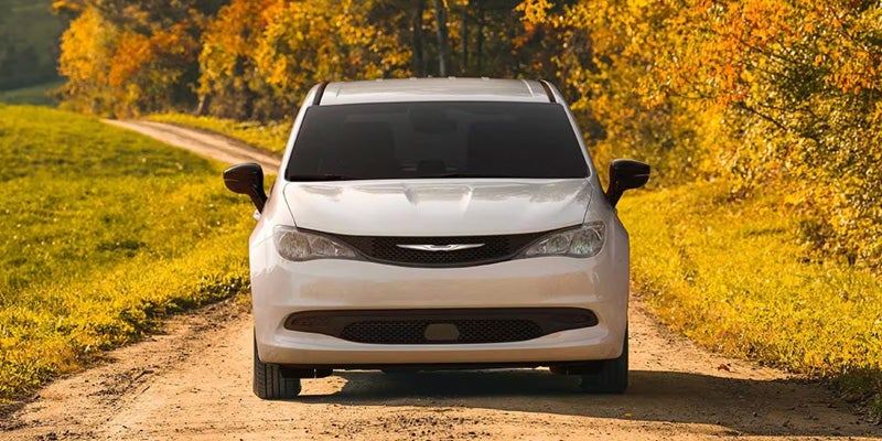 Front view of a white minivan parked on a dirt road with autumn trees