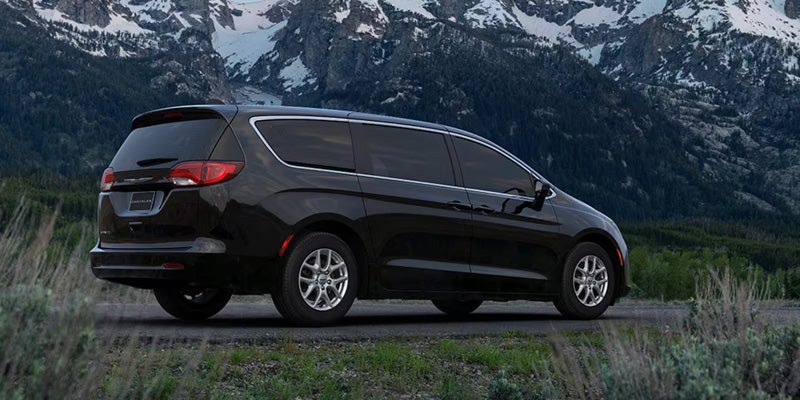 Black minivan parked on a roadside with mountains and greenery in the background