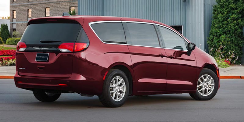 Red minivan driving on a city street, shown from rear three-quarter view