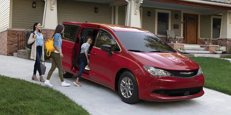 Red minivan parked in a driveway with people entering through the open sliding door near a house