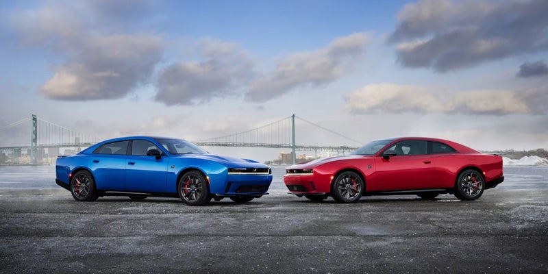 Blue and red sports sedans parked side by side outdoors with a city bridge in the background