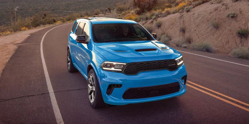Bright blue performance SUV driving on a winding road through a desert landscape