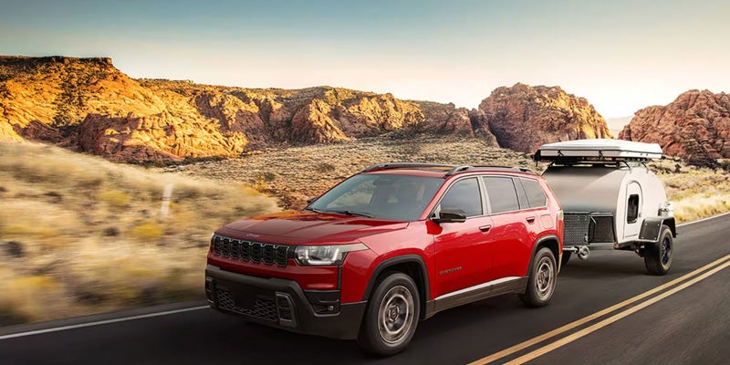 Red SUV driving on a desert road towing a small camper trailer