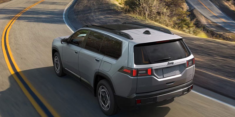 Gray SUV driving along a winding road surrounded by hills, shown from a rear angle