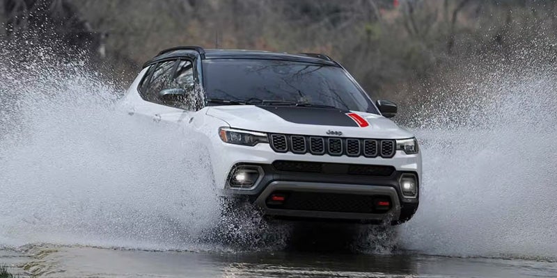 White Jeep SUV driving through shallow water, creating large splashes on both sides