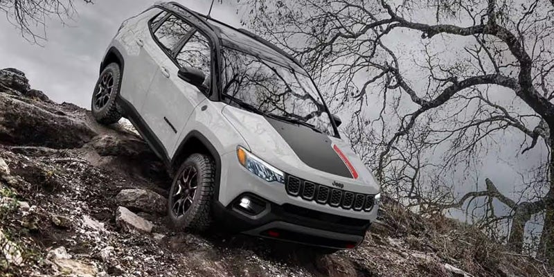 White SUV climbing a steep rocky trail with uneven terrain and trees in the background