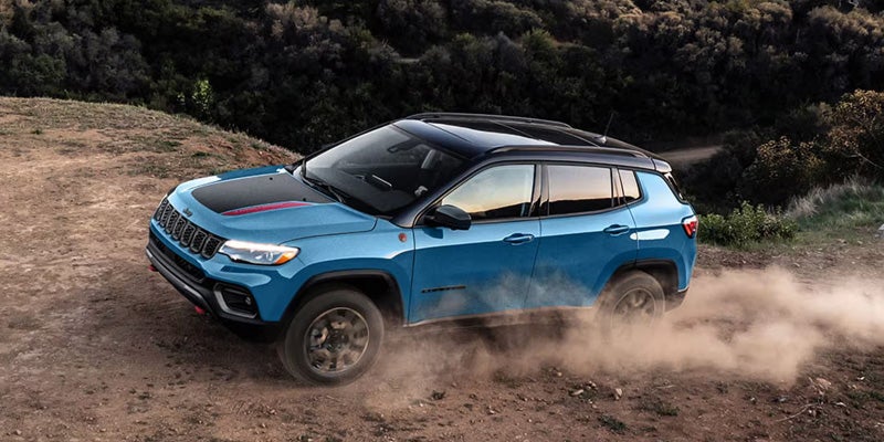 Blue SUV driving on a dirt path kicking up dust, surrounded by rugged terrain