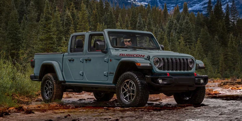 Green Jeep Gladiator Rubicon pickup truck parked on a rocky forest trail