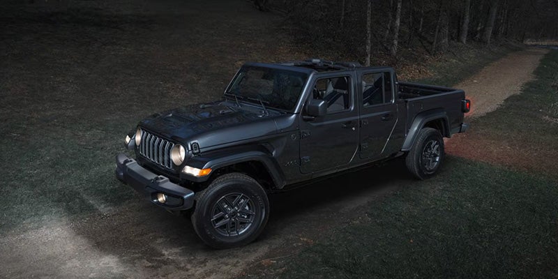 Black Jeep pickup driving off-road at night with headlights illuminating a dirt trail