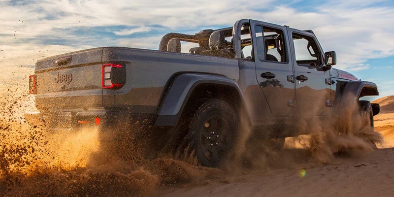 Jeep pickup truck driving on dirt terrain, kicking up dust behind it
