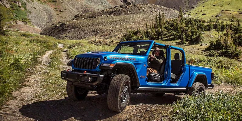 Blue Jeep pickup truck off-roading on a mountain trail with doors removed