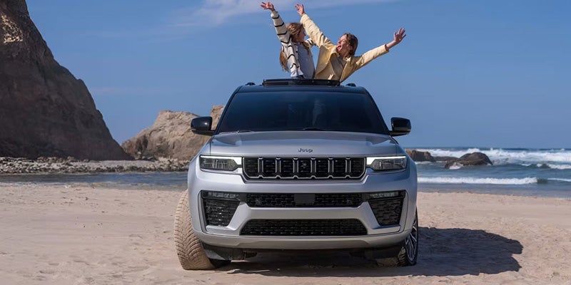 White SUV parked on a beach with passengers visible through the sunroof
