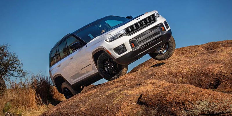 White SUV climbing a rocky incline, showing off-road capability on uneven terrain under a clear sky