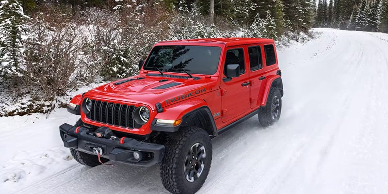 Red four-door Jeep Wrangler Rubicon driving on a snowy forest road