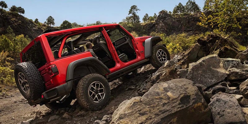 Red two-door Jeep Wrangler Rubicon rock crawling over large boulders on a rugged trail
