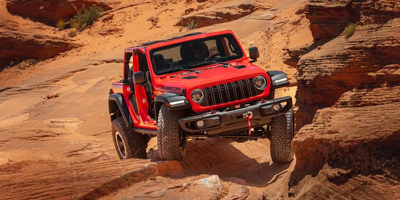 Red Jeep Wrangler Rubicon navigating a sandy desert canyon