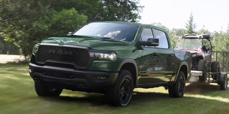 Green RAM pickup truck driving on grass while towing a trailer carrying an off-road vehicle