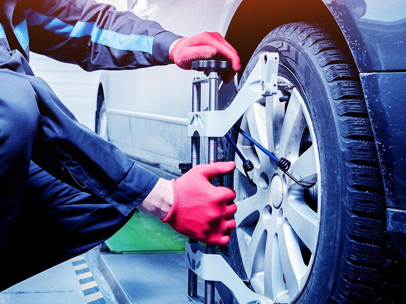 Mechanic in red gloves performing a wheel alignment on a car using specialized equipment.
