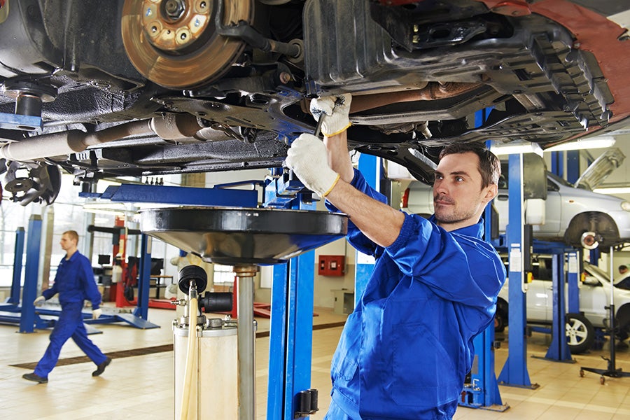 A mechanic in blue coveralls uses a wrench under a lifted car